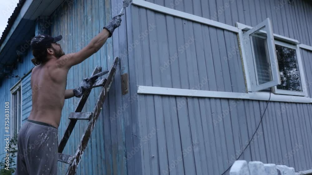 male painter paints a wooden house gray with a brush male painter paints a wooden house gray with a brush