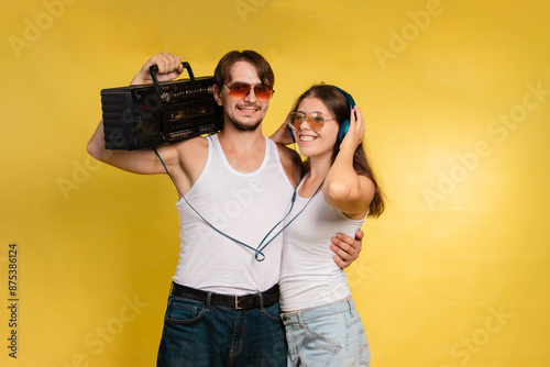 Young man and woman in sunglasses on yellow background. Retro style. Man has retro tape recorder. Listening to music