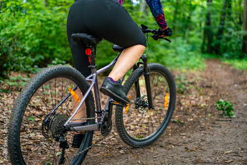 Cycling training in forest. Young woman in colorful blouse and black shorts riding bike on forest path. Playing sports outdoors in spring. Healthy lifestyle. Back view
