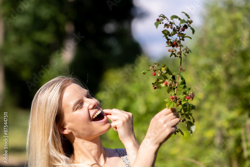 Young beautiful woman eating wild raspberries in the forest