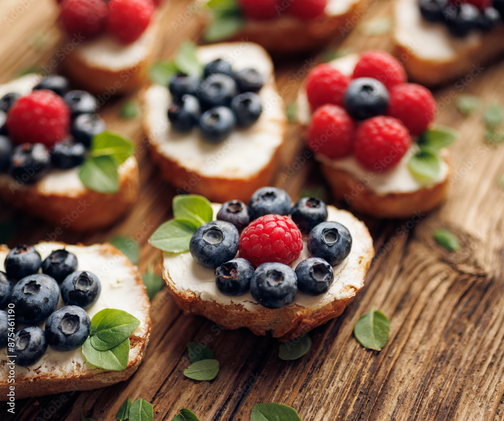 Small baguette toasts crostini with berry fruits and sweet creamy cheese on a wooden background, focus on the toast with blueberries and raspberry, close-up Small baguette toasts crostini with berry fruits and sweet creamy cheese on a wooden background, focus on the toast with blueberries and raspberry, close-up