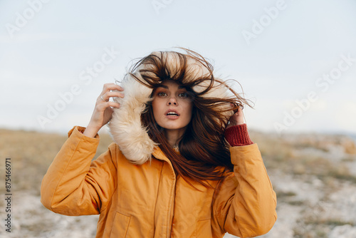 Foto Young woman in a yellow coat enjoying the breezy beach as her hair flows in the