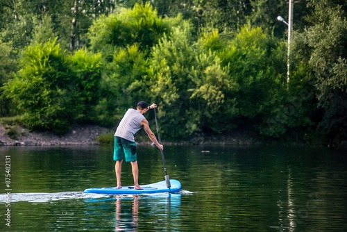 A man sup surfing paddling on a boat on the river in summer.