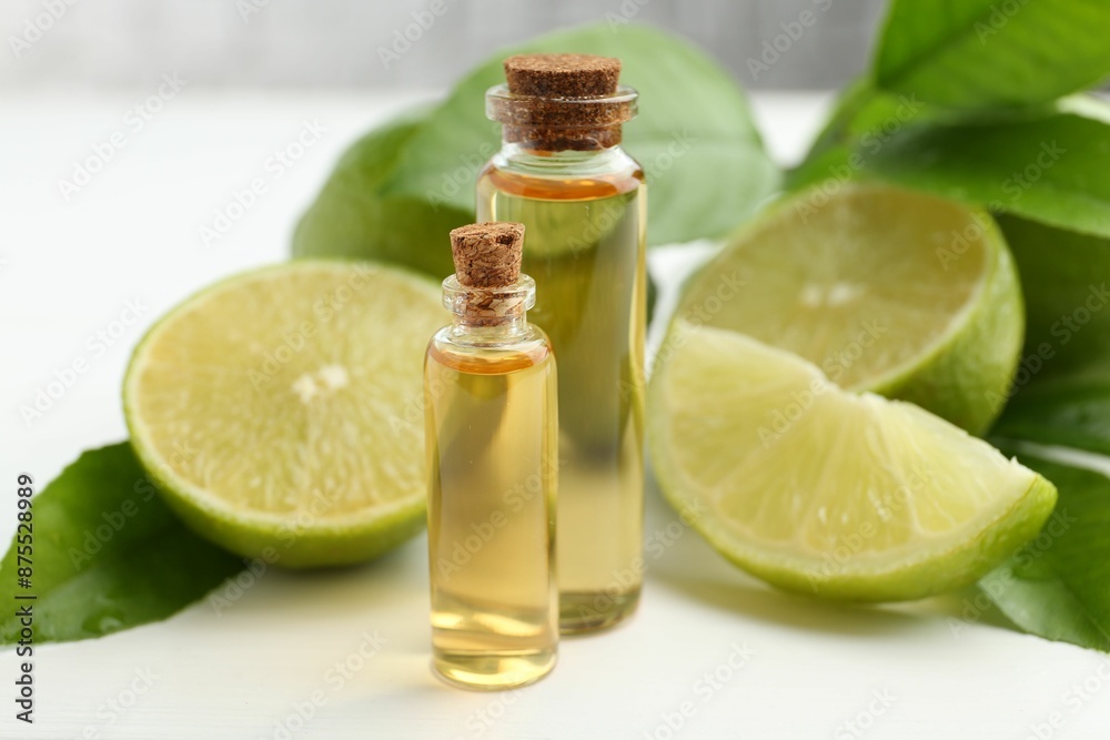 Essential oils in bottles, limes and green leaves on white table, closeup Essential oils in bottles, limes and green leaves on white table, closeup