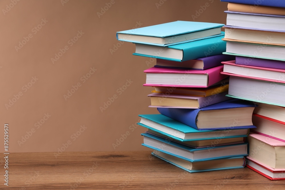 Stacks of colorful books on wooden table against light brown background, space for text Stacks of colorful books on wooden table against light brown background, space for text