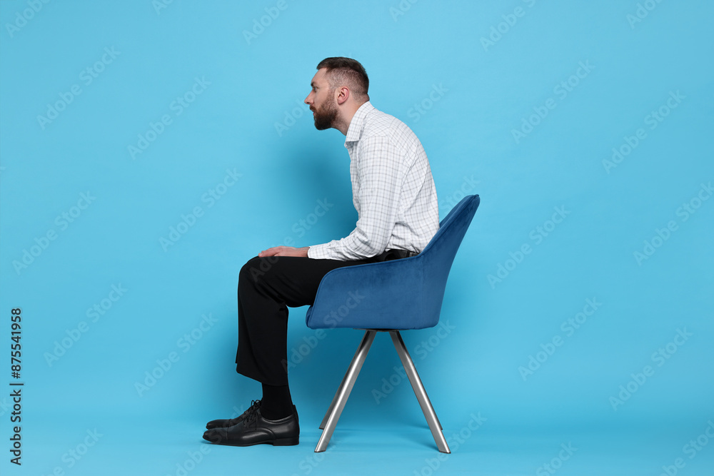 Man with poor posture sitting on chair against light blue background Man with poor posture sitting on chair against light blue background