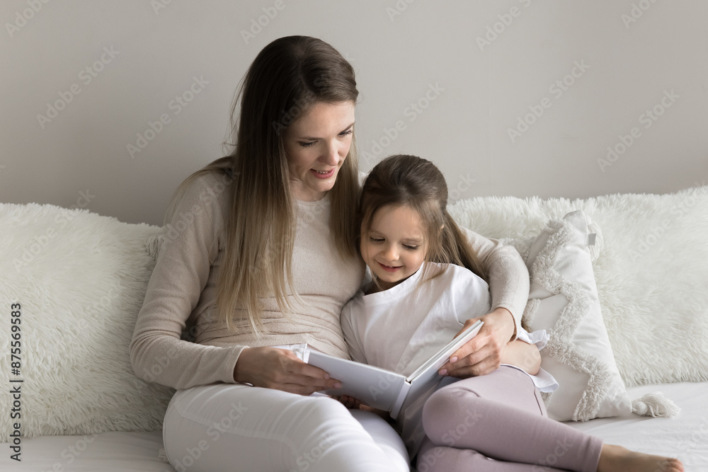 Loving young mother sit with little daughter, spend leisure time together at home with paper book, read interesting fairytale, enjoy favourite hobby. Children development, education, good life habit Loving young mother sit with little daughter, spend leisure time together at home with paper book, read interesting fairytale, enjoy favourite hobby. Children development, education, good life habit