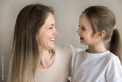 Close up side profile faces view of young 30s loving mother and beautiful preschooler daughter smiling looking at each other with tenderness and love. Happy motherhood, carefree childhood, family ties