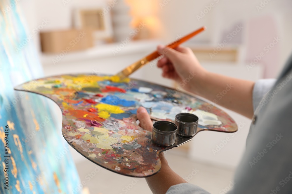 Fototapeta premium Woman mixing paints on palette with brush near easel indoors, closeup