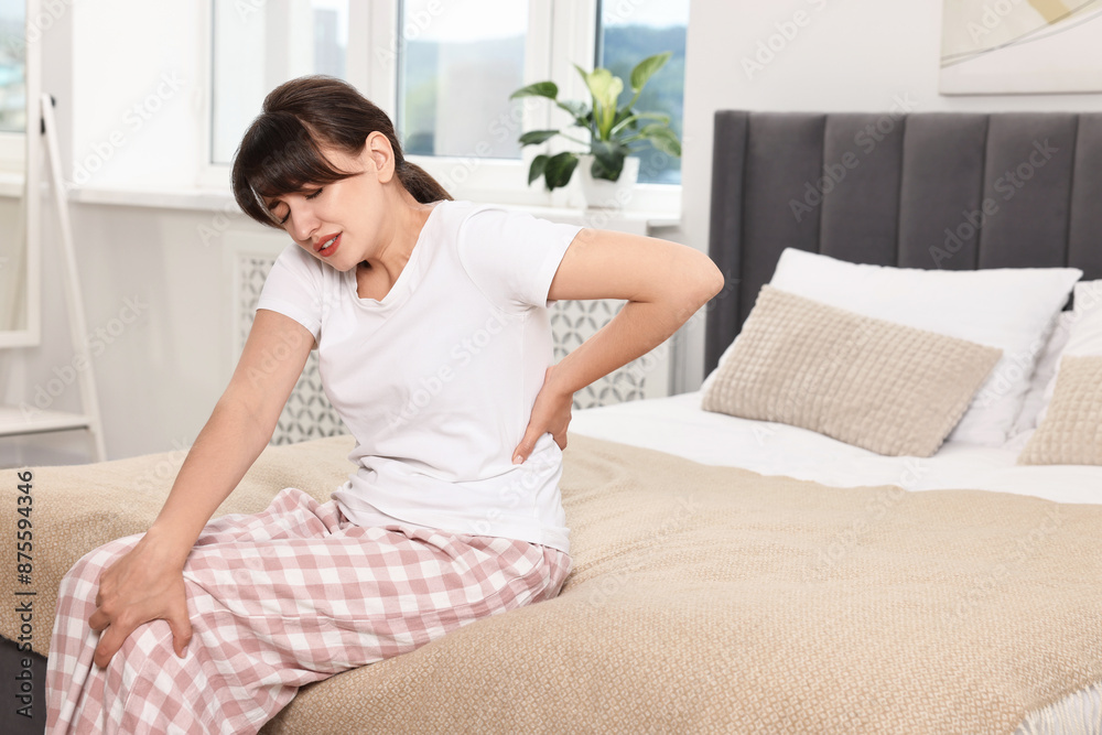 Upset woman suffering from back pain on bed at home Upset woman suffering from back pain on bed at home