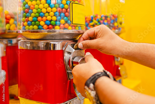 Bild auf Leinwand Close-up of a man's arms and hands inserting a coin into an orange and yellow gumball machine