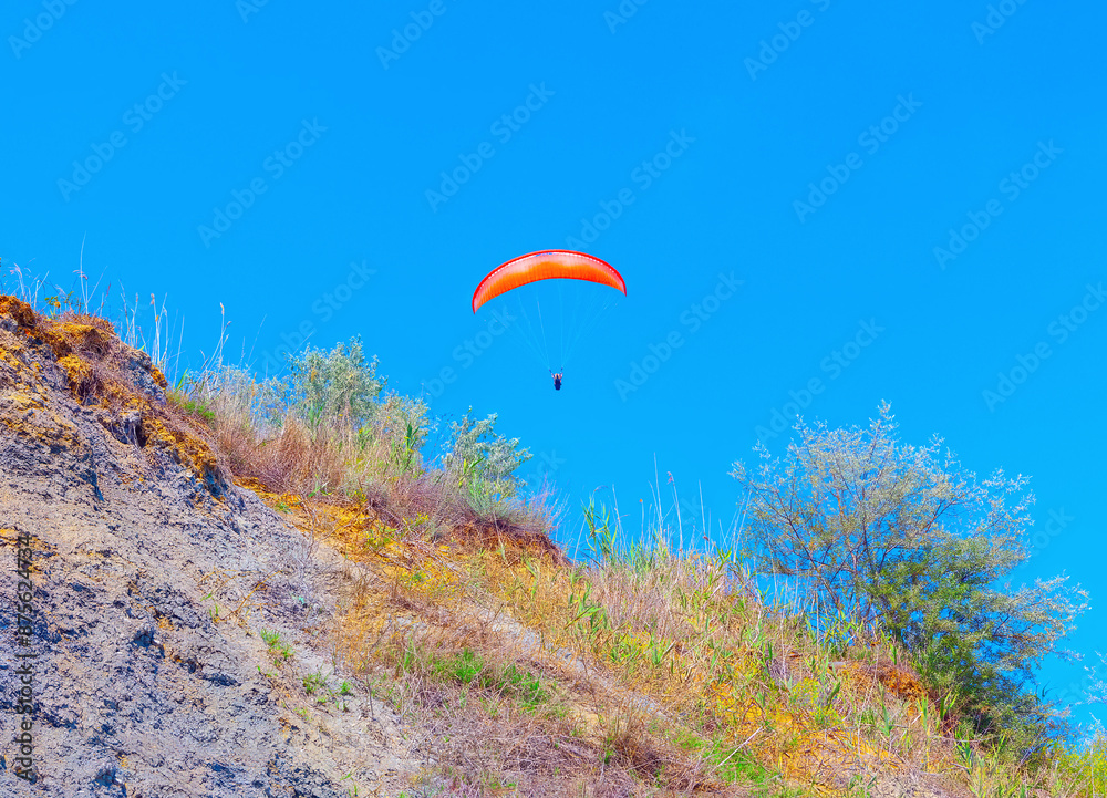 Paragliding over a hill. Person is flying a parachute on a hill Paragliding over a hill. Person is flying a parachute on a hill