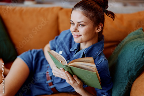Fotografie Woman relaxing at home on a cozy couch while engrossed in a book reading session