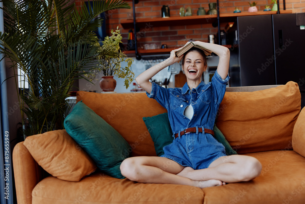 Obraz premium Happy woman sitting on orange couch with hands on head smiling and relaxed in living room
