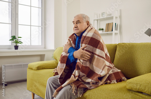 Fotografie Upset senior man covered with blanket sitting on sofa