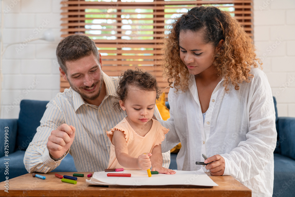 Fototapeta premium Enjoy happy smiling love family father and mother with little girl learning and writing in book with pencil making homework at home. Education concept 