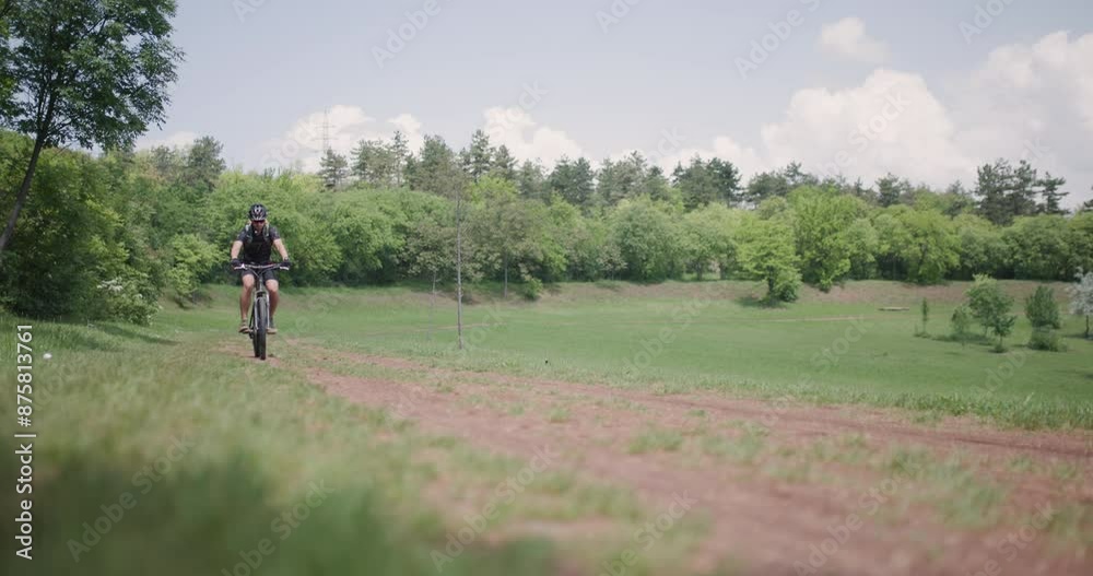 Man riding a mountainbike down a dusty path with scenic countryside views. Dirtroad next to a green meadow. 50 fps on cinema camera. Man riding a mountainbike down a dusty path with scenic countryside views. Dirtroad next to a green meadow. 50 fps on cinema camera.