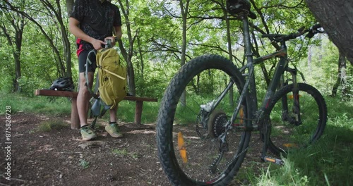 Mountain biker sitting on a bench in the forest. Standing and getting his mountainbike. Adventurer ready for action. photo