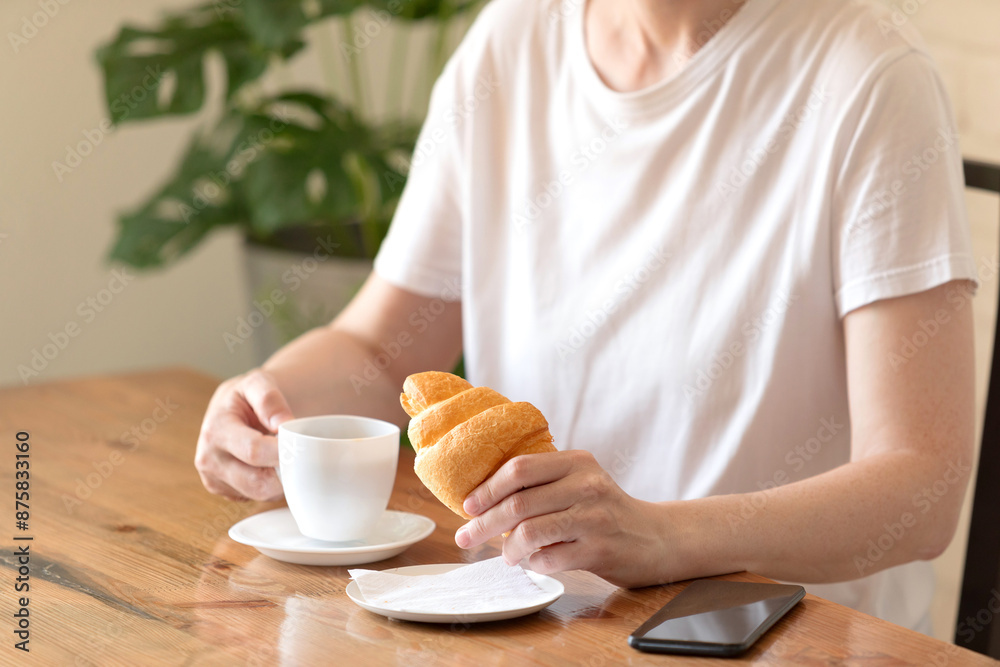 Woman in a white T-shirt with a cup of coffee and a croissant at a table in a café Woman in a white T-shirt with a cup of coffee and a croissant at a table in a café