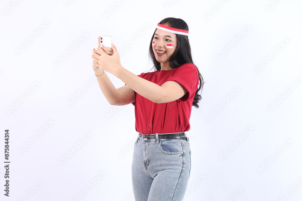 Excited young Asian woman holding mobile phone with selfie isolated over white background. Celebrate Indonesian independence day on 17 August