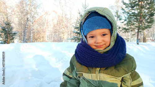 A young boy bundled up in a warm winter jacket and hat smiles for the camera against a snowy backdrop. The childs rosy cheeks and bright eyes indicate they are enjoying the cold weather.