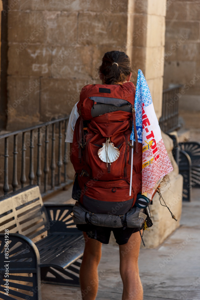Fototapeta premium Detail shot of a pilgrim on his back with his large backpack on his back and the characteristic shell of the Camino de Santiago.