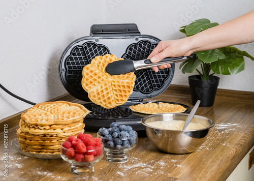 Making Belgian waffles. Female hand pours dough into waffle maker in kitchen at home. Cooking summer breakfast with round waffles and berries photo