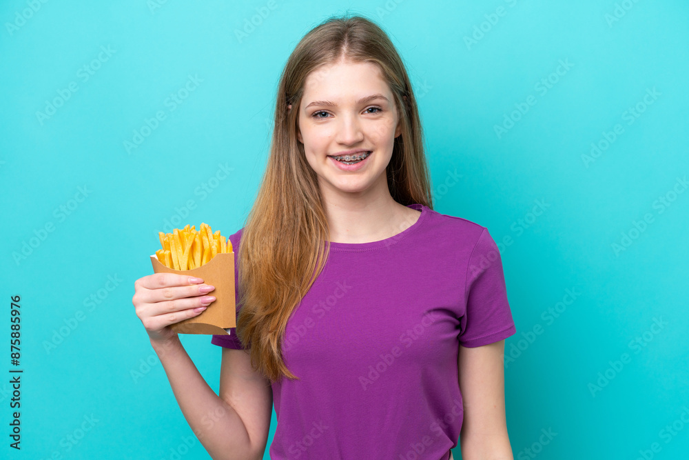 Teenager Russian girl catching french fries isolated on blue background smiling a lot Teenager Russian girl catching french fries isolated on blue background smiling a lot