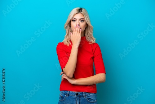 Young Russian woman isolated on blue background covering mouth with hand
