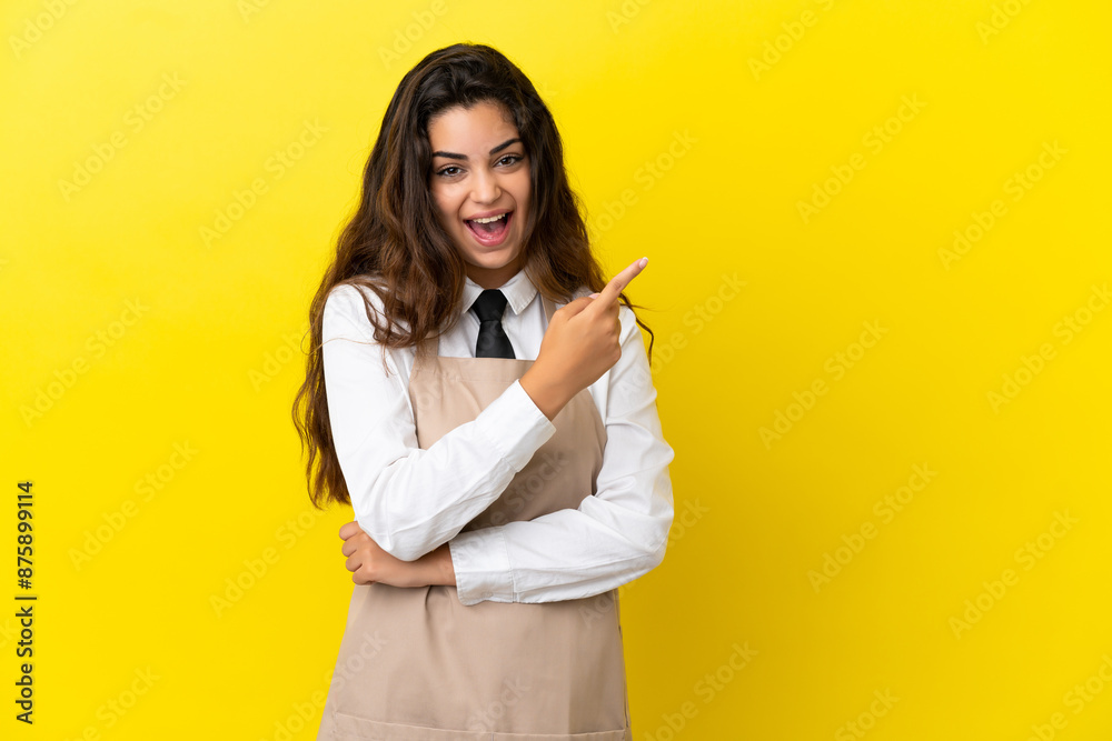 Young caucasian restaurant waiter isolated on yellow background surprised and pointing side Young caucasian restaurant waiter isolated on yellow background surprised and pointing side