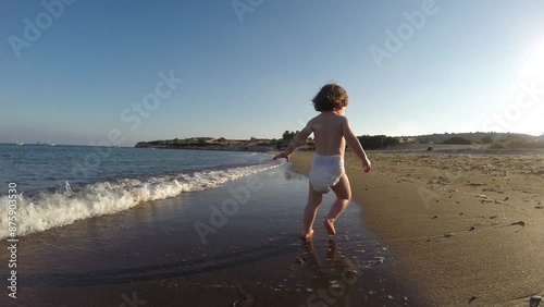  Slow motion of toddler baby girl in nappy running on sandy beach  through sea waves
