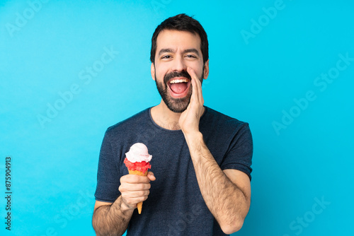 Young man with a cornet ice cream over isolated blue background shouting with mouth wide open photo