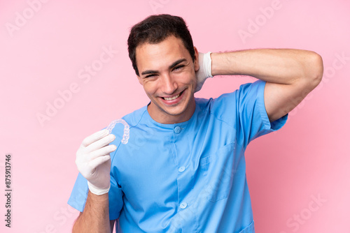 Dentist caucasian man holding invisible braces isolated on pink background laughing