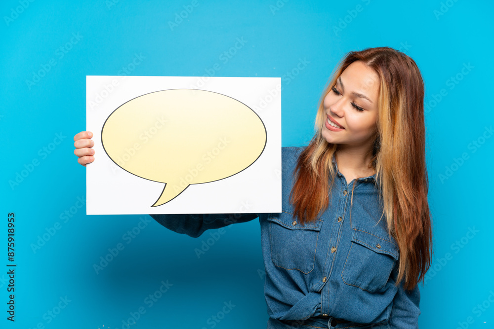 Teenager girl over isolated blue background holding a placard with speech bubble icon Teenager girl over isolated blue background holding a placard with speech bubble icon