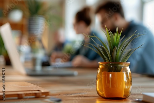 Close-up of potted plant on an office desk with blurred people in the background, creating a calm and productive workspace atmosphere. photo