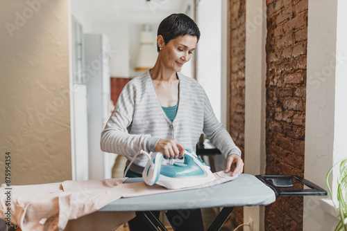 Cuadro en lienzo Indoor portrait of happy smiling pretty mature mother ironing washed and dry clo