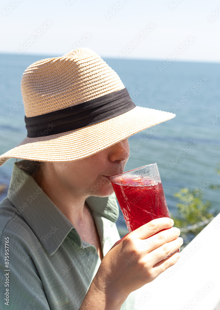a young woman in a straw hat drinks a cocktail against the background of the sea a young woman in a straw hat drinks a cocktail against the background of the sea