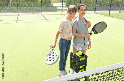 Blonde girl teaching another girl how to hold a paddle racquet on an outdoor paddle court on a sunny day