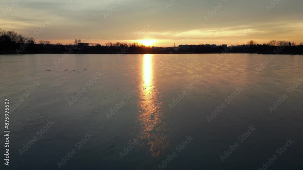 Tranquil sunset over a serene frozen lake, reflecting the sun golden light on the ice surface. Silhouetted trees and buildings in the distance add depth. Tranquil sunset over a serene frozen lake, reflecting the sun golden light on the ice surface. Silhouetted trees and buildings in the distance add depth.
