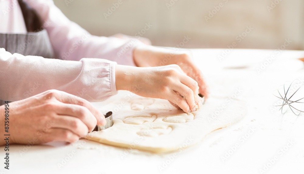 A close-up photo of a woman and a child cutting out shapes from dough using cookie cutters. They are working together in a kitchen environment. The woman is on the left, the child is on the right. A close-up photo of a woman and a child cutting out shapes from dough using cookie cutters. They are working together in a kitchen environment. The woman is on the left, the child is on the right.