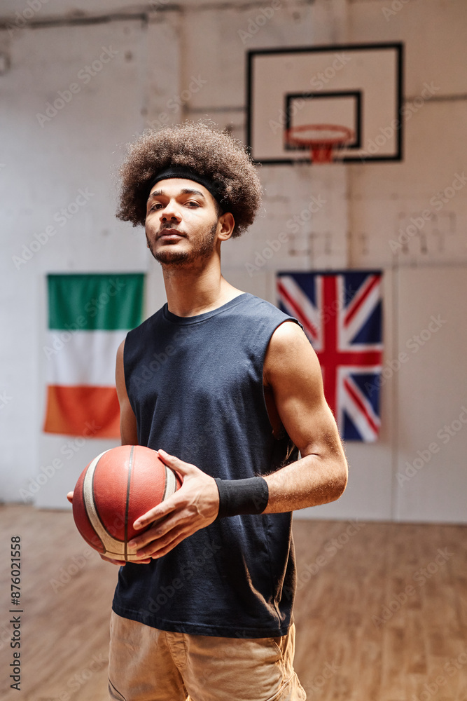 Vertical portrait of teenage African American boy as a basketball player holding ball and looking at camera in dramatic light Vertical portrait of teenage African American boy as a basketball player holding ball and looking at camera in dramatic light