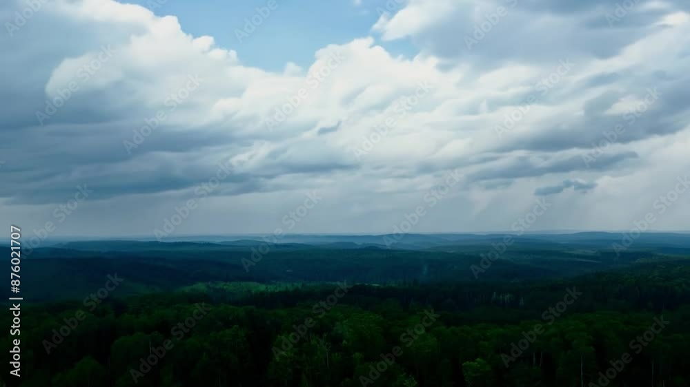 From a drone, the timelapse captures the cloudy sky passing over a lush, green forest during the day. From a drone, the timelapse captures the cloudy sky passing over a lush, green forest during the day.