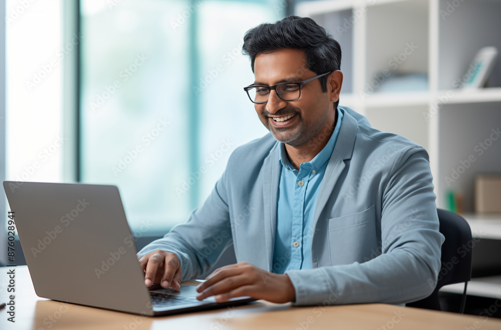 A professional man in a light blue jacket, smiling as he works on his laptop in a modern office setting with a bright and airy background A professional man in a light blue jacket, smiling as he works on his laptop in a modern office setting with a bright and airy background