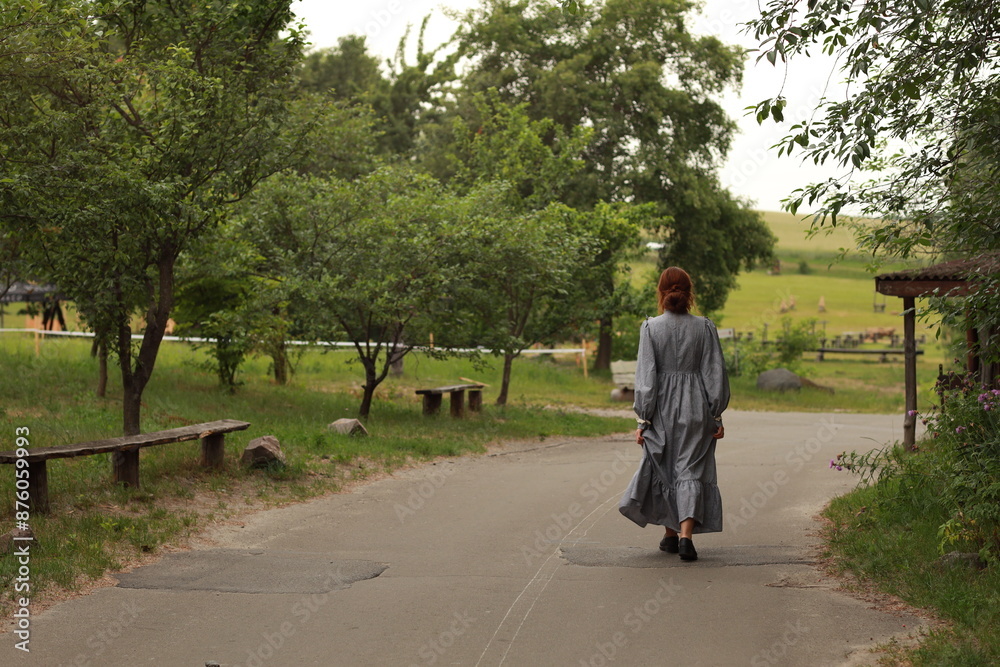 Fototapeta premium Young woman in old fashioned dress walking by the road from back