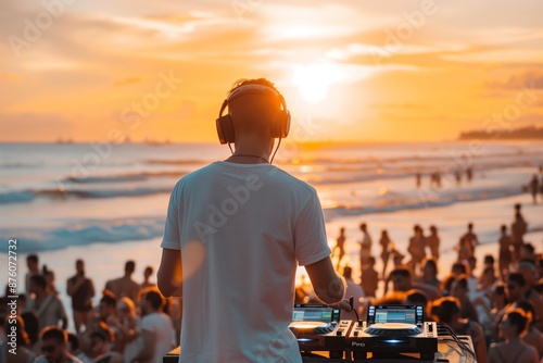 Obraz na płótnie A DJ performs in front of a large crowd at a beach party during sunset. The sun is setting over the ocean, and the waves are crashing in the background. w salonie
