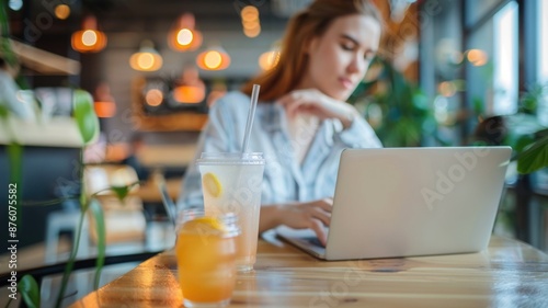 A woman working on her laptop in a cozy cafe with a refreshing drink in the foreground.