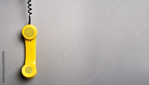 Yellow telephone handset hanging on light grey background. Space for text  photo