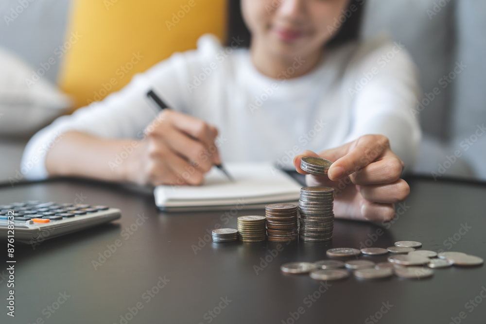 Financial, asian young woman, girl putting stack coins on table for calculate cost sitting in living room at home, financial plans to spend enough money on his income for saving money and payment. Financial, asian young woman, girl putting stack coins on table for calculate cost sitting in living room at home, financial plans to spend enough money on his income for saving money and payment.