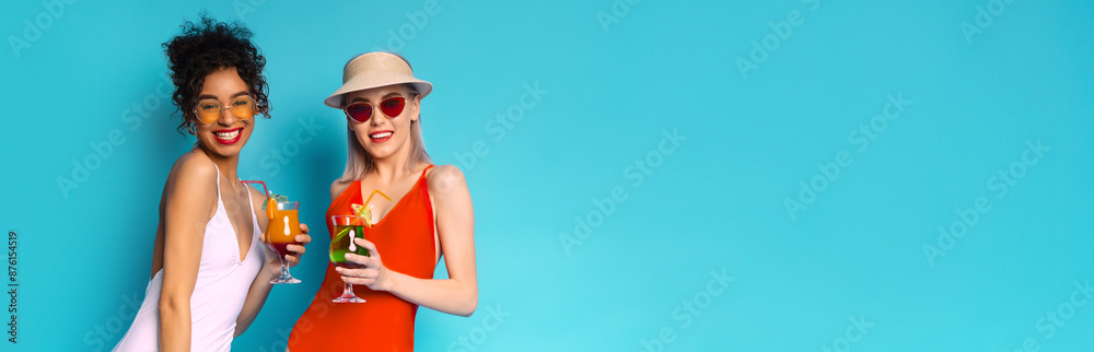 Two multiracial women smiling and holding colorful drinks in front of a bright blue background, enjoying their summer drinks and are looking happy and relaxed, copy space Two multiracial women smiling and holding colorful drinks in front of a bright blue background, enjoying their summer drinks and are looking happy and relaxed, copy space