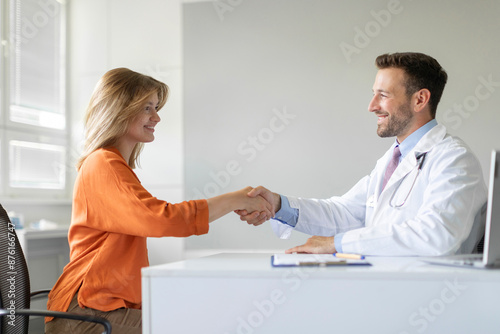 Friendly male GP shaking hand of female patient during first consultation in clinic, man handshaking woman client, closing health insurance deal, side view © Home-stock